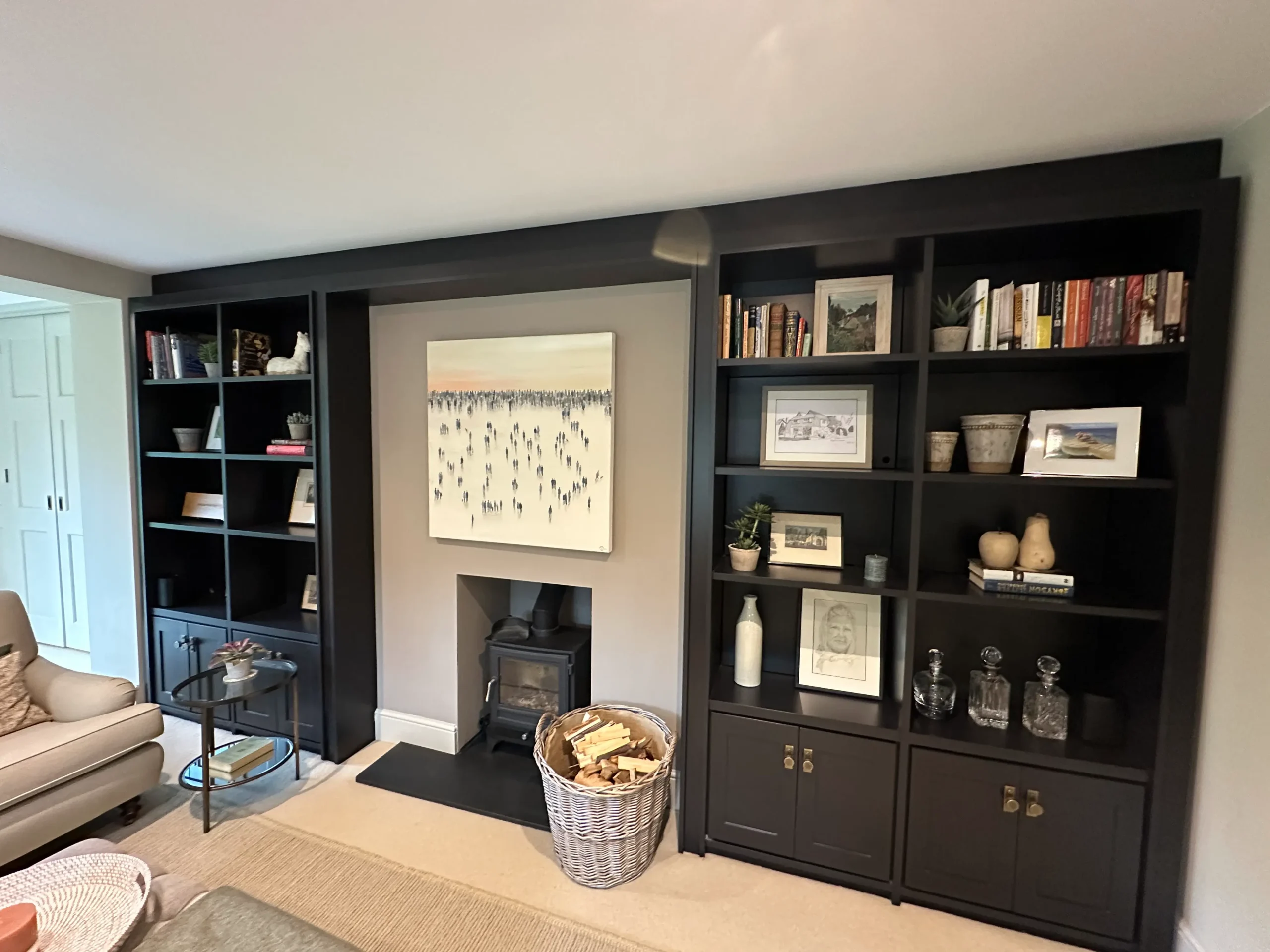 A bespoke joinery dark grey library shelving and cupboards, to store items such as books, ornaments and photo frames, shown in a lounge in a home.