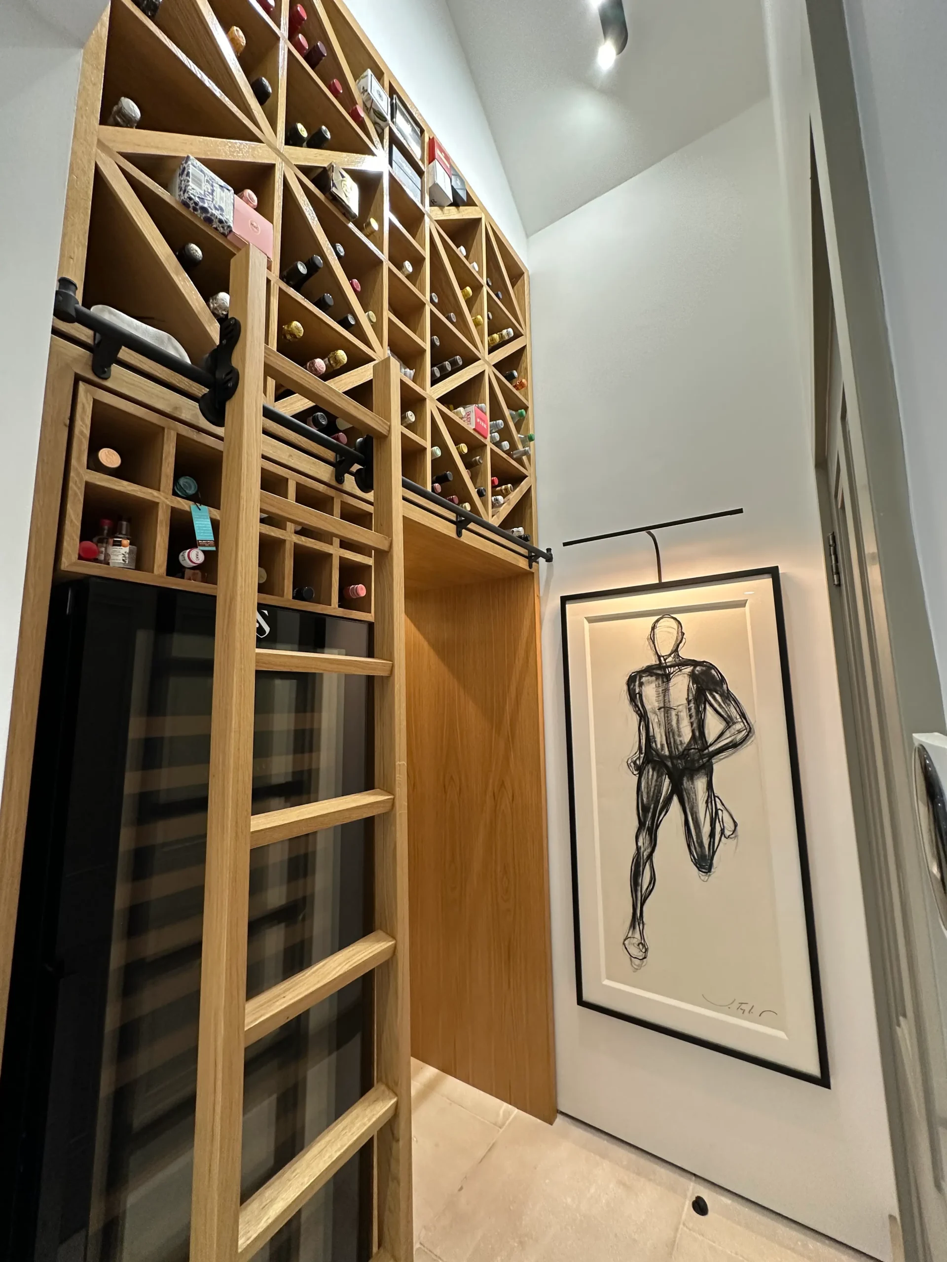 Beautiful oak wine cellar shelving with a ladder to reach the highest shelves, created by luxury bespoke joinery.