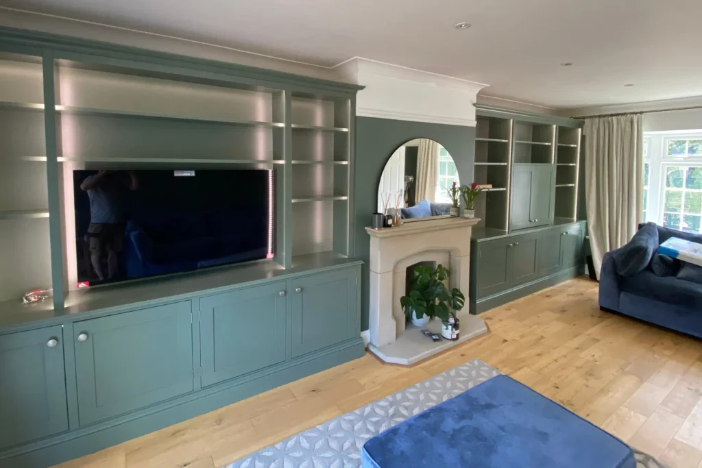 Exceptional bespoke joinery sage green shelves and cupboards, for a television, books, ornaments and other possessions.
