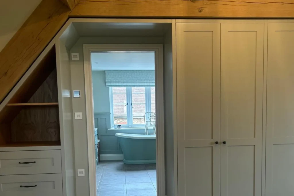Sage green bespoke fitted wardrobes in a bedroom with oak beams and an ensuite